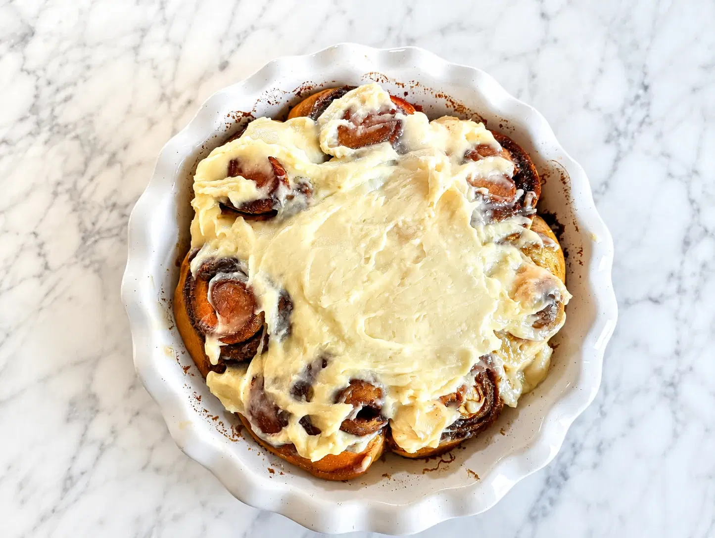 Soft sweet potato sourdough cinnamon rolls with cream cheese frosting in a baking dish